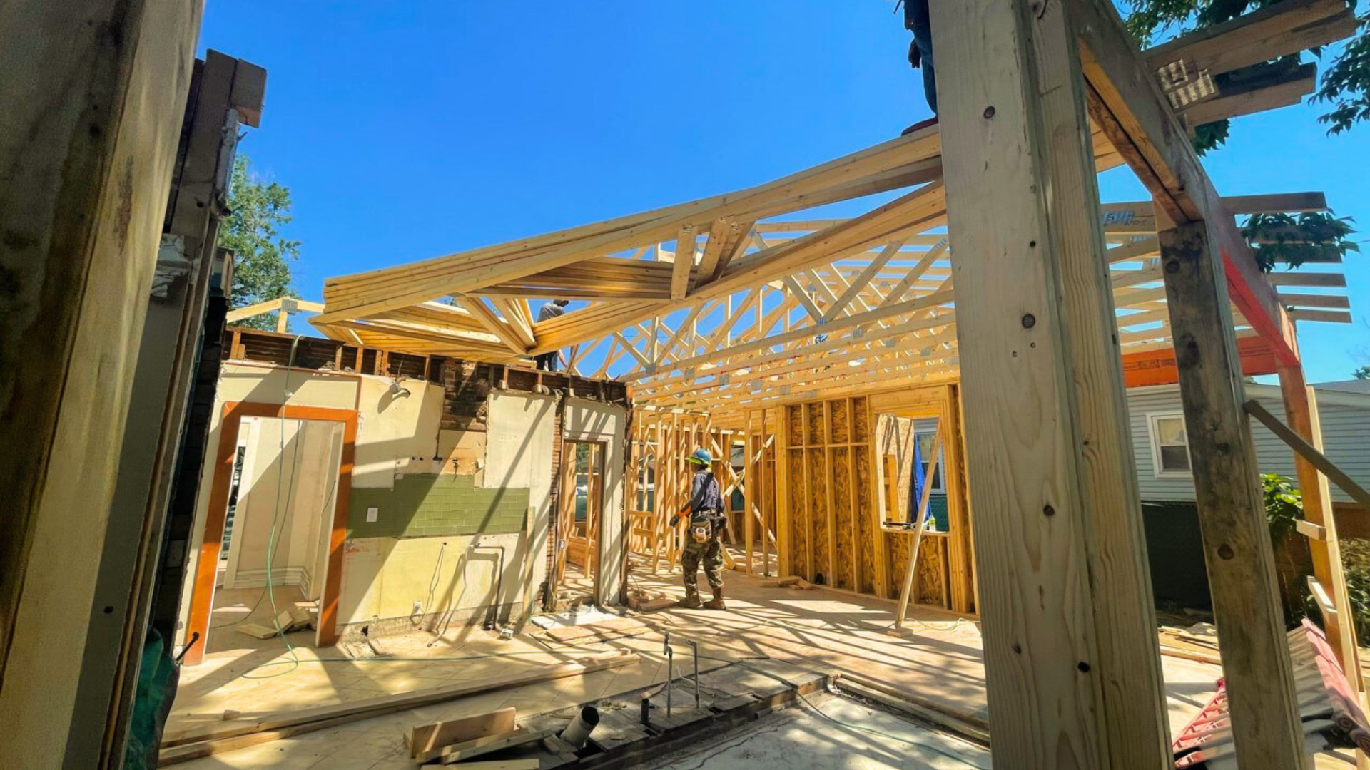 Sustainable Design Build home remodeling in progress showing a man standing in a home that is being framed with trusses and wood beams