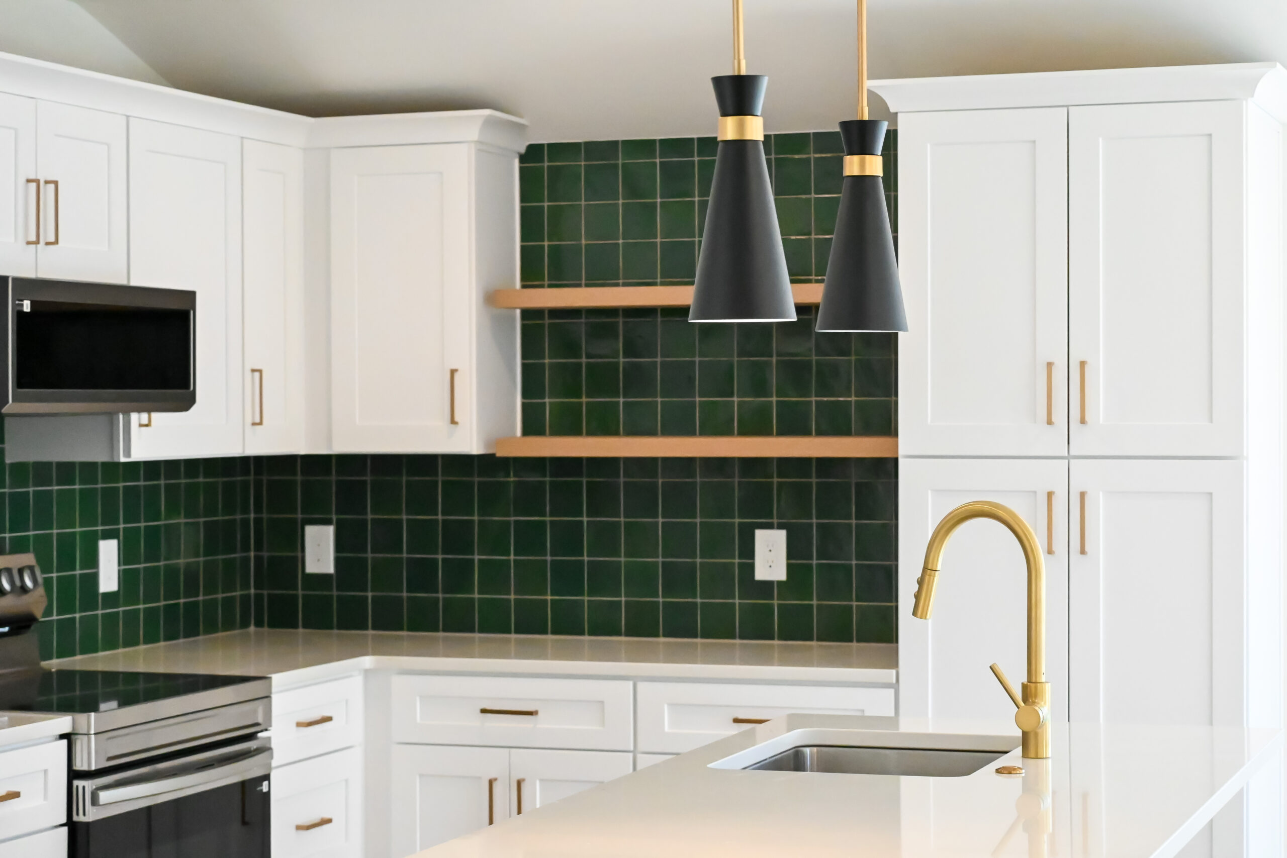 Beautiful well-lit ADU home kitchen in Denver built by Sustainable Design Build complete with emerald green subway tile backsplash gold faucet and hardware white cabinetry